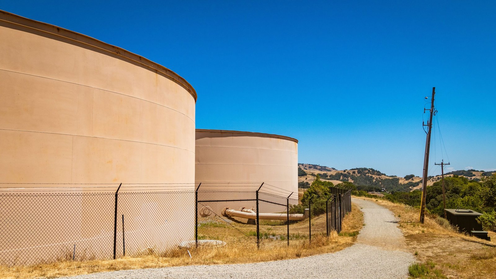 Large storage tanks in a rural landscape with hills under clear blue skies.