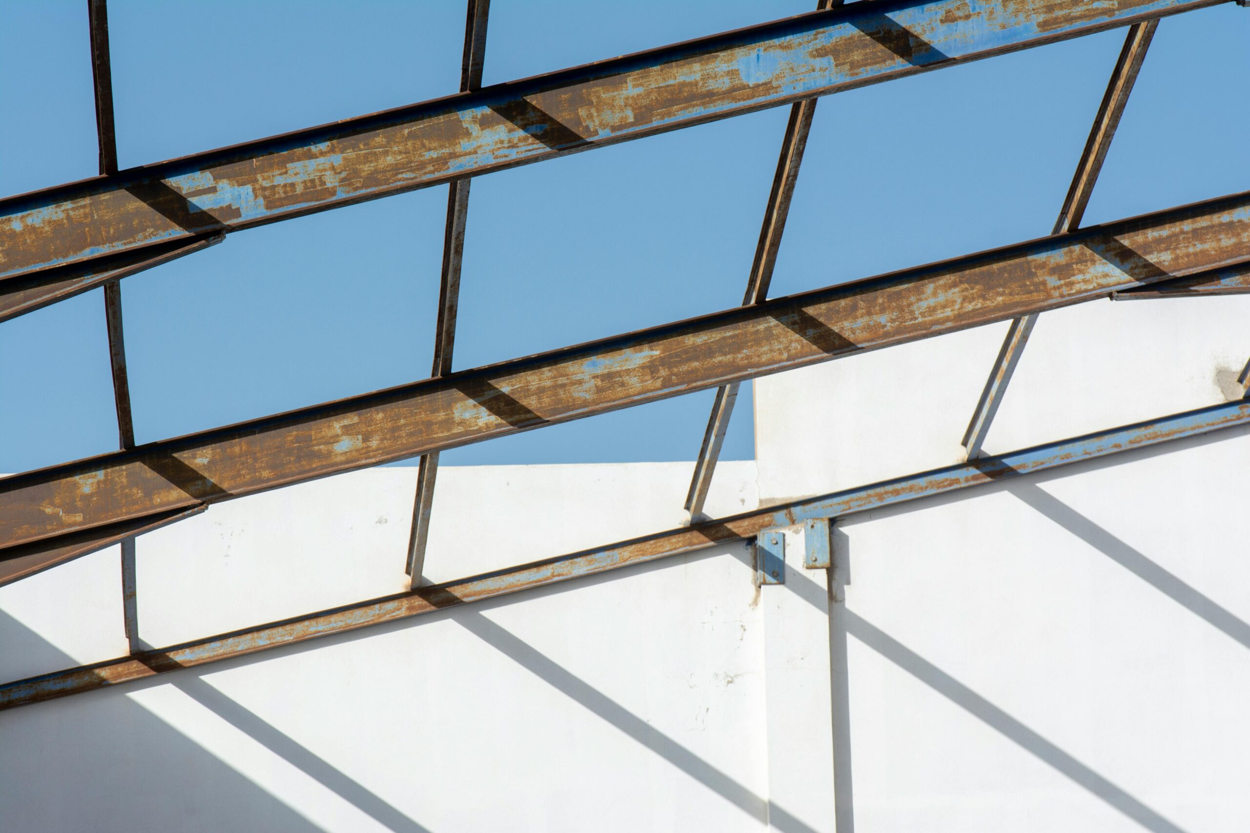 Rusty metal beams create geometric patterns against a clear blue sky.